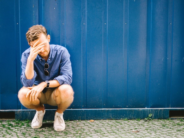 Uomo depresso accovacciato contro il muro blu