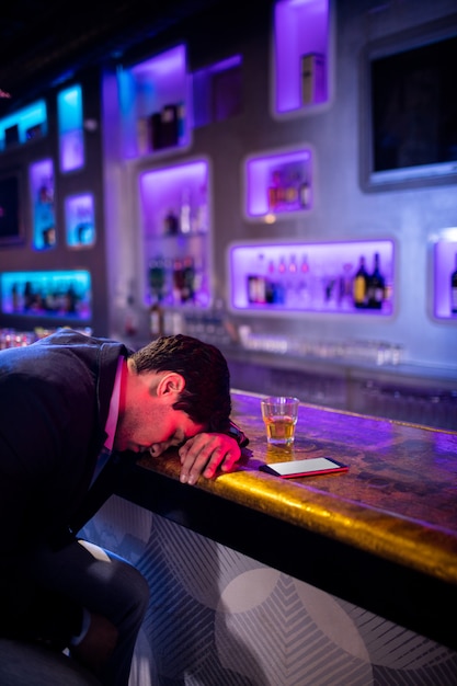 Uomo depresso che mangia whisky al bancone del bar