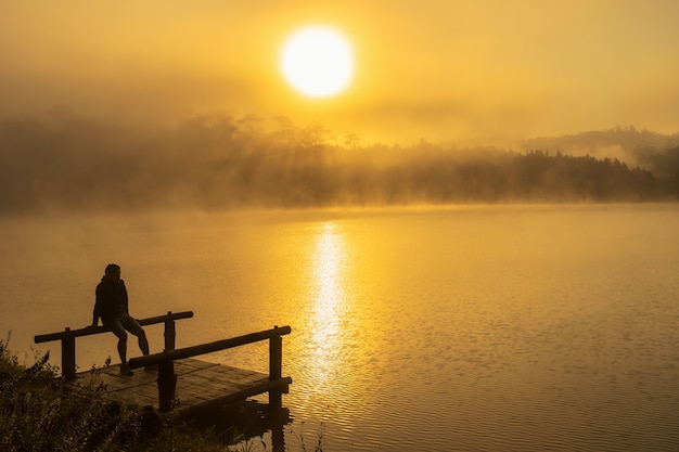 Uomo depresso della siluetta che si siede sul lago del fiume della casa galleggiante