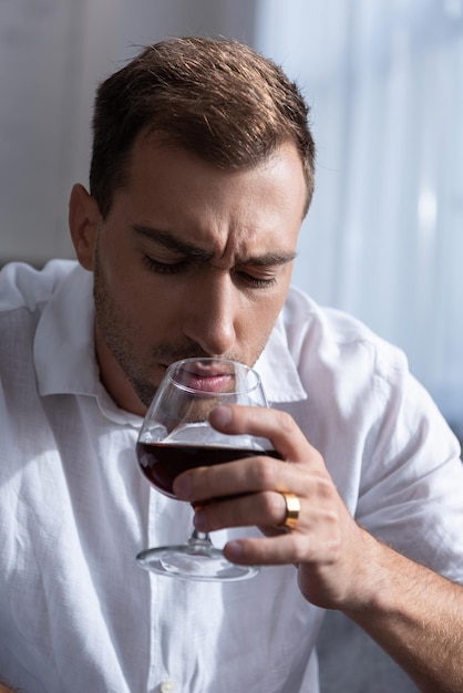 Uomo depresso in camicia che beve cognac a casa