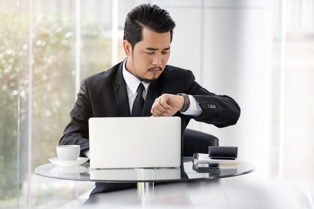 Uomo di affari che controlla tempo sull'orologio astuto mentre per mezzo del computer portatile