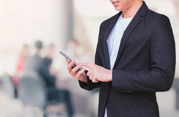 Uomo di affari che utilizza Smart Phone nel fondo dello spazio ufficio e nello spazio della copia.