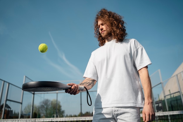 Uomo di angolo basso che gioca con la pagaia di tennis