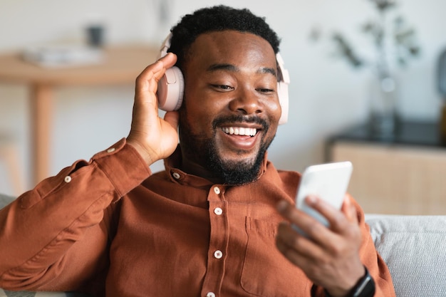 Uomo di colore che ascolta la musica che indossa le cuffie che tengono il cellulare a casa