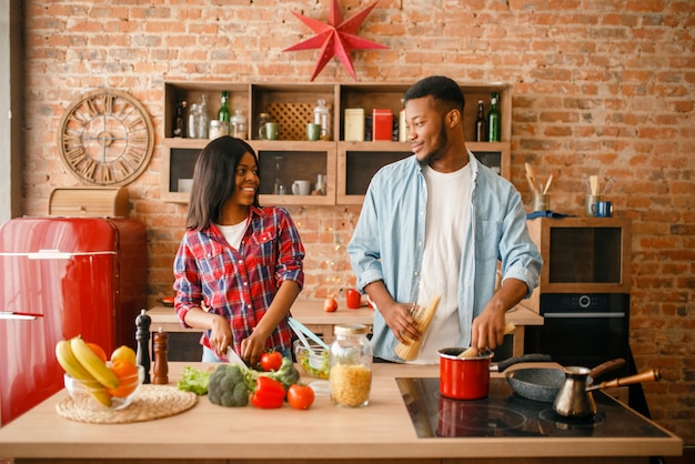 Uomo di colore che cucina sulla cucina, moglie beve caffè