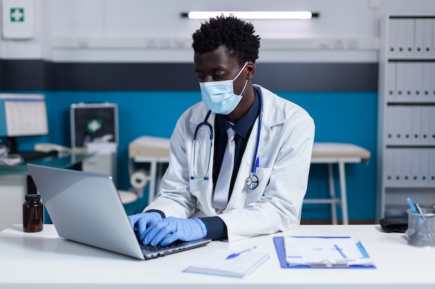 Uomo di colore con occupazione medico che utilizza laptop sulla scrivania