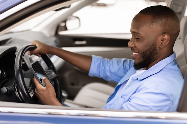 Uomo di colore felice che usa lo smartphone che guida l'auto