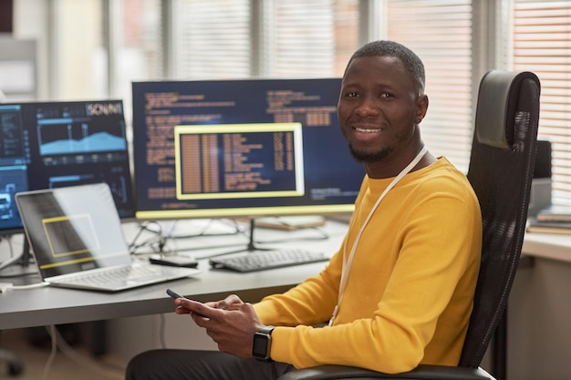 Uomo di colore sorridente che guarda l'obbiettivo sul posto di lavoro nello sviluppo di software