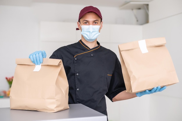 Uomo di consegna che tiene un sacchetto di carta con cibo su sfondo bianco, fattorino di cibo in maschera protettiva.