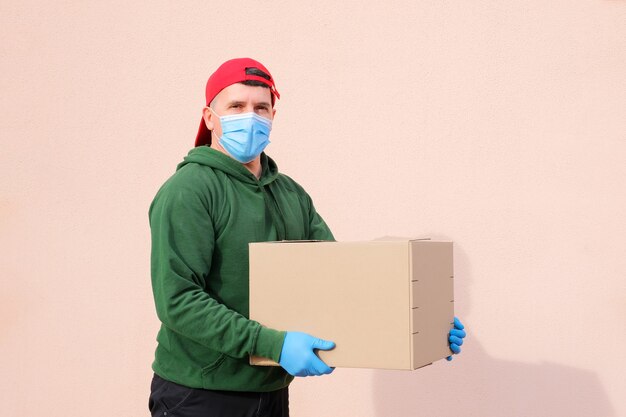 Uomo di consegna in mascherina medica e guanti che tengono e che trasportano un cardbox