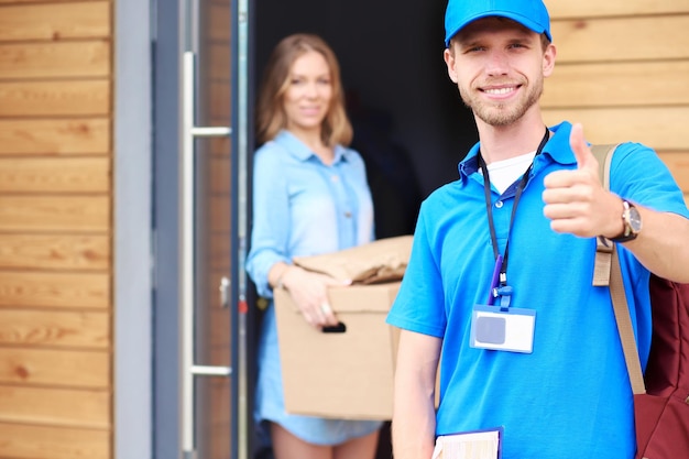 Uomo di consegna sorridente in uniforme blu che consegna la scatola dei pacchi al concetto di servizio di corriere del destinatario Uomo di consegna sorridente in uniforme blu