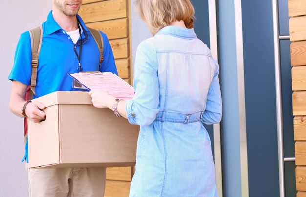 Uomo di consegna sorridente in uniforme blu che consegna la scatola dei pacchi al concetto di servizio di corriere del destinatario Uomo di consegna sorridente in uniforme blu