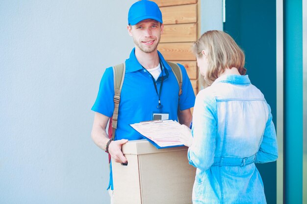 Uomo di consegna sorridente in uniforme blu che consegna la scatola dei pacchi al concetto di servizio di corriere del destinatario Uomo di consegna sorridente in uniforme blu