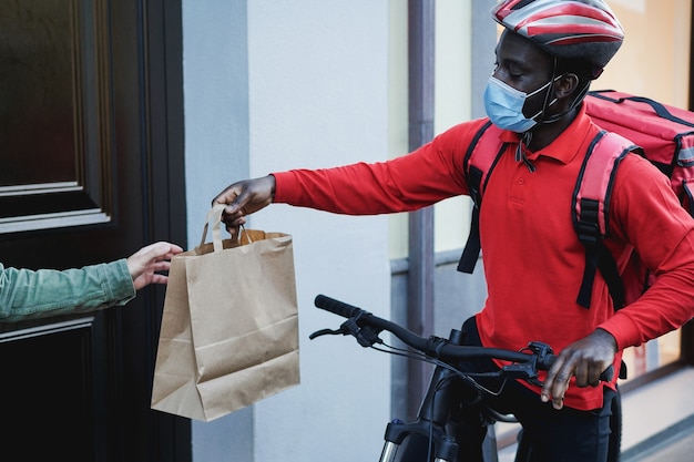 Uomo di corriere africano con zaino termico e bici che suona il campanello per il servizio di consegna - Focus sul viso