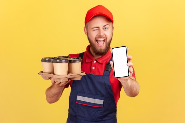 Uomo di corriere che tiene smartphone con pizza a schermo vuoto e caffè da asporto che strizza l'occhio alla fotocamera