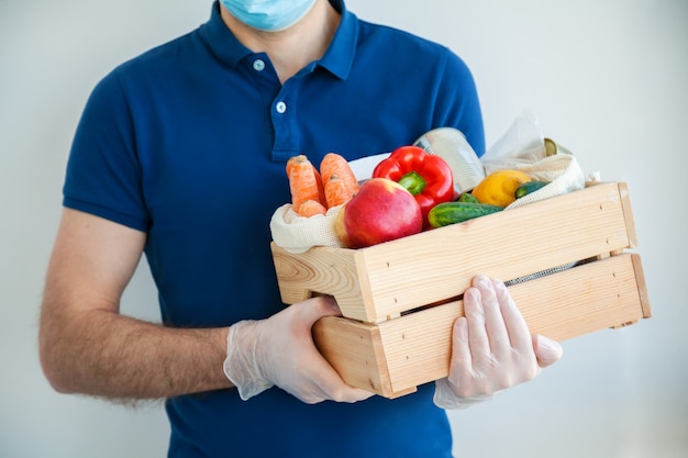 Uomo di corriere in guanti protettivi in possesso di una scatola piena di cibo