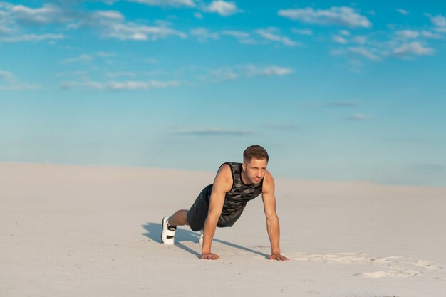 Uomo di forma fisica che fa le esercitazioni nel deserto della sabbia.