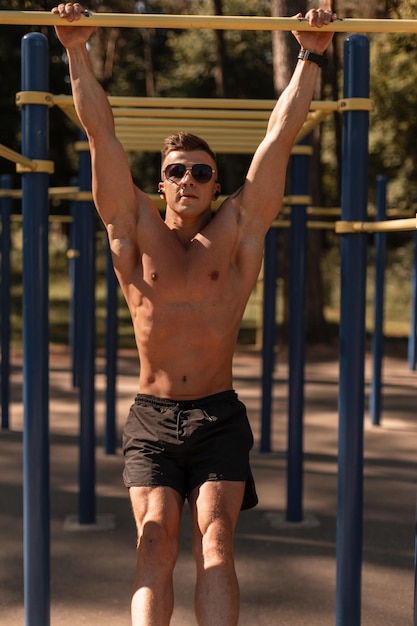 Uomo di forma fisica con un corpo muscoloso forte che fa gli allenamenti dello stomaco sulla barra orizzontale all'aperto
