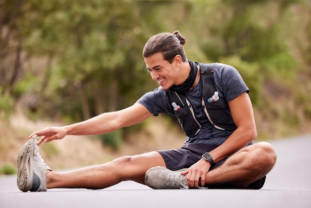 Uomo di forma fisica e allungamento delle gambe per l'allenamento di corsa o l'esercizio nella natura all'aperto Sorriso maschio attivo felice nel riscaldamento delle gambe per iniziare la corsa di allenamento sportivo o l'esercizio su strada o su strada