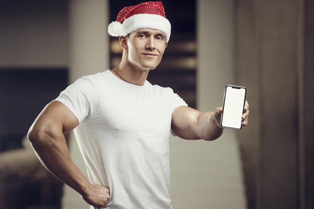 Uomo di forma fisica in costume del cappello di Babbo Natale in palestra con il telefono cellulare. Buon Natale e Anno Nuovo concetto