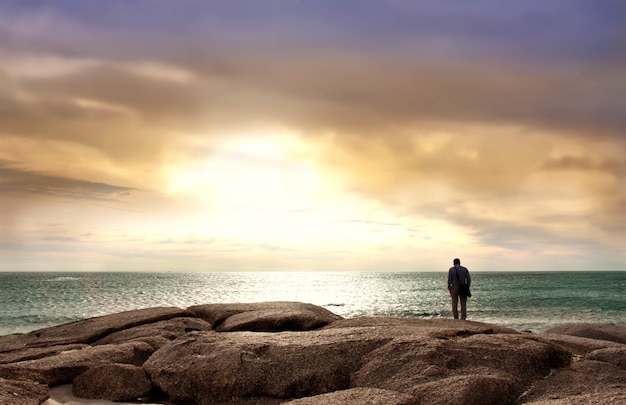 Uomo di fronte mare in piedi su pietre di mare