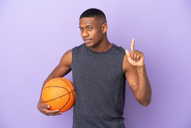 Uomo di giovane giocatore di basket latino isolato sulla parete viola che mostra e alzando un dito in segno del meglio