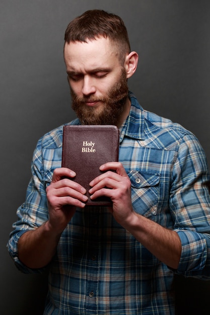 Uomo di Handsone che legge e che prega sopra la Bibbia in una stanza buia sopra struttura grigia