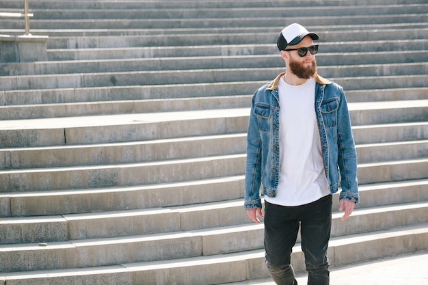 Uomo di hipster che cammina indossando jeans neri, t-shirt e un berretto da baseball