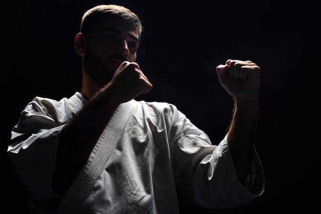 Uomo di karate in un kimono in posizione di combattimento su sfondo nero