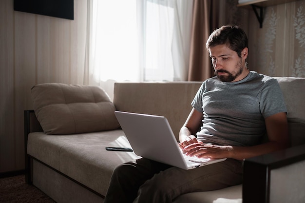 Uomo di lavoro a distanza che lavora al computer portatile seduto sul divano di casa