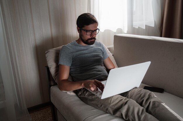 Uomo di lavoro a distanza che lavora al computer portatile seduto sul divano di casa