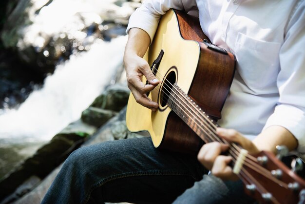 Uomo di metà sezione che suona la chitarra mentre è seduto vicino al fiume