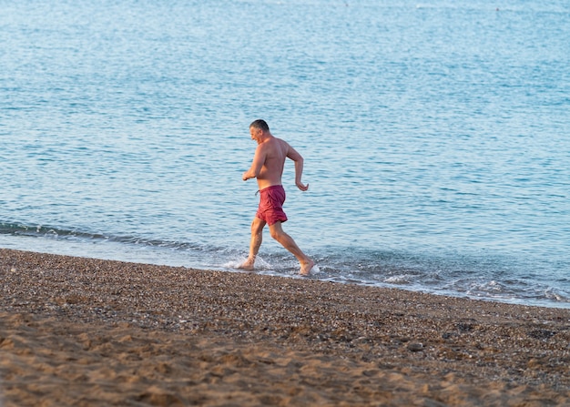 Uomo di mezza età atletico che fa jogging lungo una spiaggia nel surf