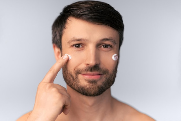 Uomo di mezza età che applica la crema sul viso sullo sfondo bianco