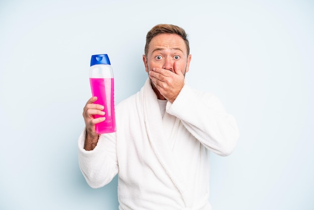 Uomo di mezza età che copre la bocca con le mani con uno scioccato. bottiglia di shampoo