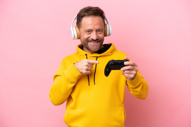 Uomo di mezza età che gioca con un controller per videogiochi isolato su sfondo rosa che punta verso il lato per presentare un prodotto