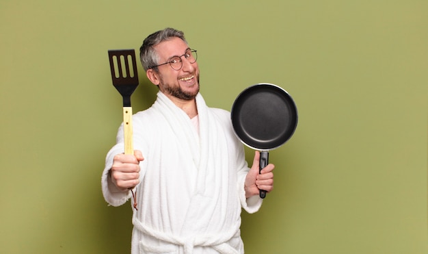 Uomo di mezza età che indossa accappatoio e impara a cucinare con una padella