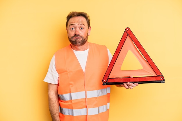 Uomo di mezza età che scrolla le spalle, sentendosi confuso e incerto.. concetto di auto con guasto a triangolo