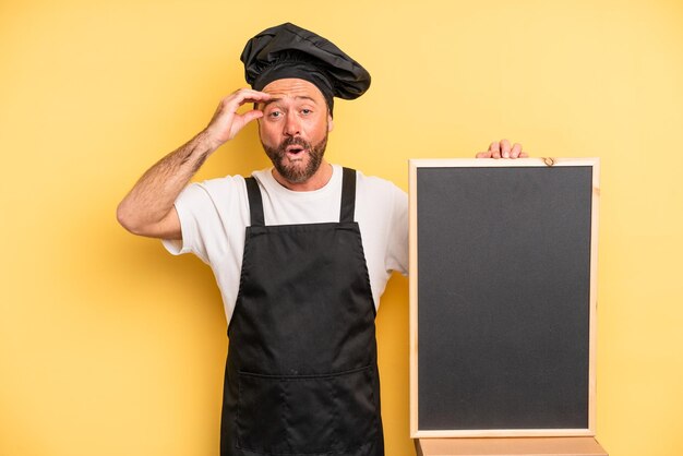 uomo di mezza età che sembra felice, stupito e sorpreso. concetto di chef e lavagna