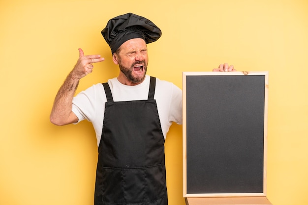 Uomo di mezza età che sembra gesto suicida infelice e stressato facendo segno di pistola chef e concetto di lavagna