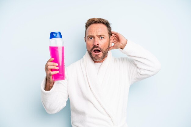 Uomo di mezza età che si sente stressato, ansioso o spaventato, con le mani sulla testa. bottiglia di shampoo