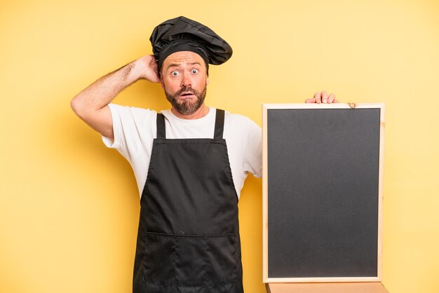 Uomo di mezza età che si sente stressato, ansioso o spaventato, con le mani sulla testa. concetto di chef e lavagna