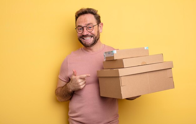 Uomo di mezza età che sorride allegramente sentendosi felice e indicando il concetto di scatole di pacchetti laterali