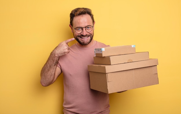 Uomo di mezza età che sorride con sicurezza indicando il proprio concetto di scatole di pacchetti con ampio sorriso