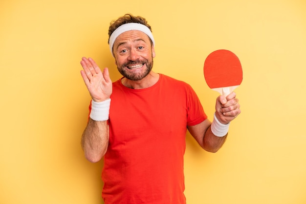 Uomo di mezza età che sorride felicemente, agitando la mano, accogliendoti e salutandoti. concetto di ping pong