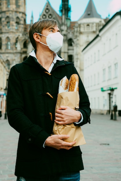 Uomo di mezza età per strada con pane, baguette, pagnotta durante la pandemia globale, indossando maschera, prendendo pane dal forno. Cibo da asporto, spesa da forno durante il covid 19.