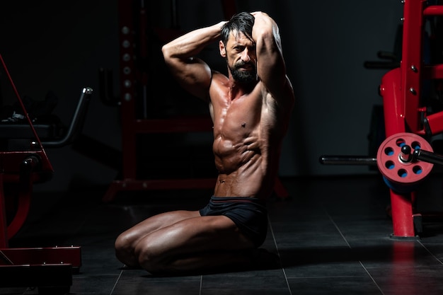 Uomo di mezza età seduto forte in palestra e flettendo i muscoli - modello di fitness bodybuilder atletico muscolare in posa dopo gli esercizi
