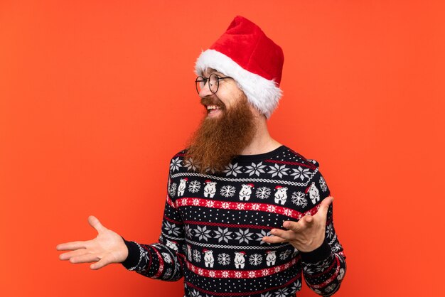 Uomo di natale con la barba lunga sopra la parete rossa isolata con espressione facciale di sorpresa