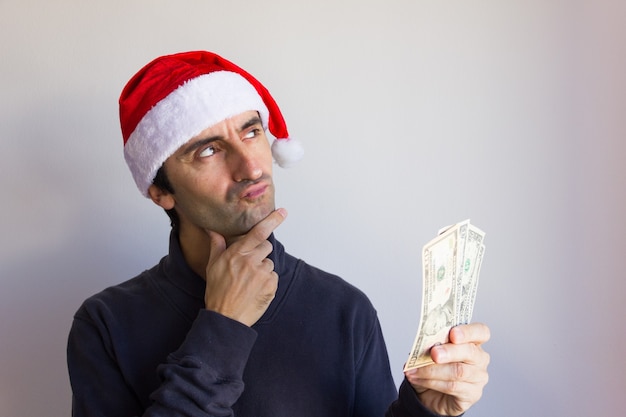 Uomo di pensiero positivo con cappello rosso di Babbo Natale che tiene le banconote in dollari su sfondo bianco