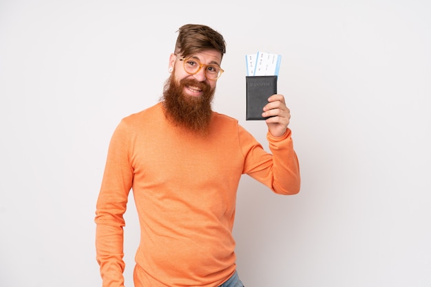 Uomo di redhead con barba lunga sul muro bianco isolato in vacanza con valigia e passaporto